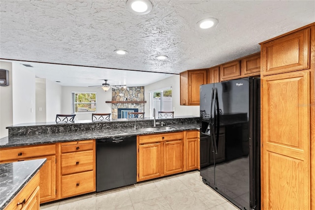 kitchen featuring sink, dark stone countertops, a fireplace, black appliances, and a textured ceiling