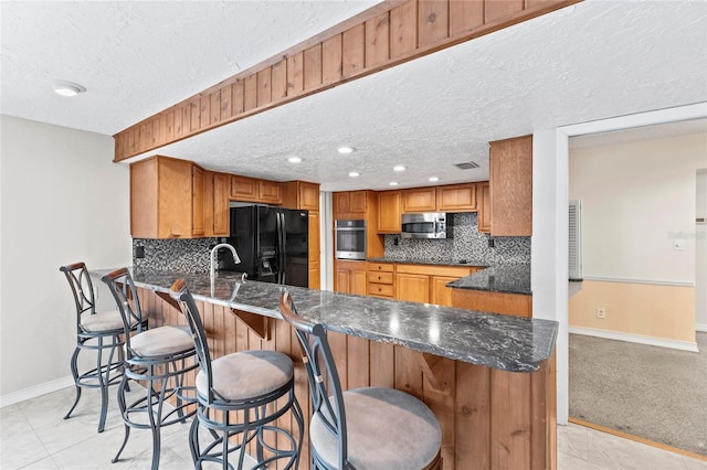 kitchen featuring a breakfast bar area, light tile patterned floors, kitchen peninsula, stainless steel appliances, and a textured ceiling