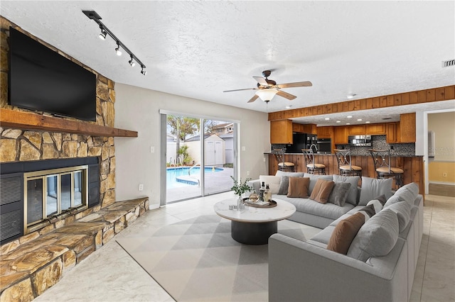 living room with a fireplace, track lighting, a textured ceiling, and ceiling fan