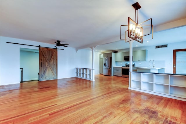 unfurnished living room featuring a barn door, ceiling fan with notable chandelier, and light hardwood / wood-style floors