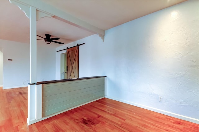 spare room featuring beam ceiling, a barn door, ceiling fan, and hardwood / wood-style floors