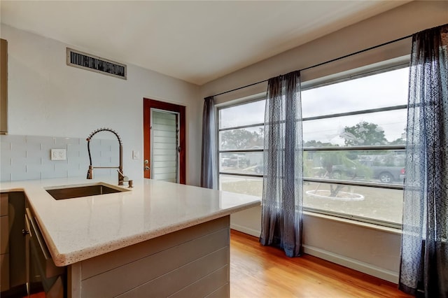 kitchen featuring light wood-type flooring, decorative backsplash, light stone counters, and sink