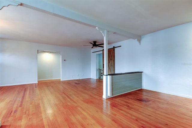 spare room featuring ceiling fan, beam ceiling, a barn door, and light hardwood / wood-style flooring