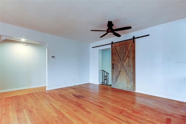 spare room with ceiling fan, a barn door, and light hardwood / wood-style floors