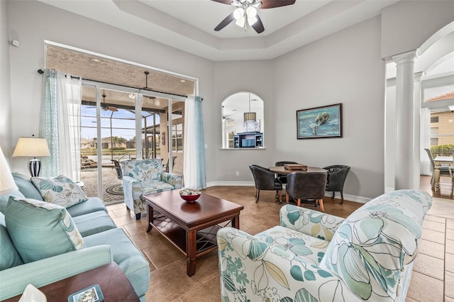 tiled living room featuring decorative columns, a tray ceiling, and ceiling fan