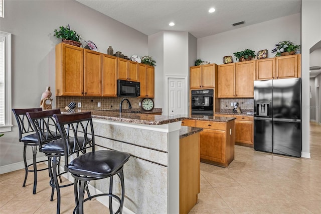 kitchen featuring light tile patterned floors, decorative backsplash, dark stone counters, a kitchen island, and black appliances