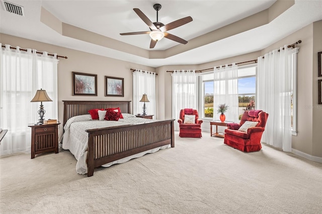 bedroom featuring ceiling fan, light colored carpet, and a tray ceiling