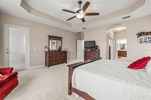 bedroom featuring ensuite bath, ceiling fan, light carpet, and a raised ceiling