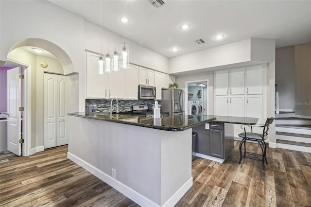 kitchen featuring white cabinets, appliances with stainless steel finishes, decorative light fixtures, backsplash, and independent washer and dryer