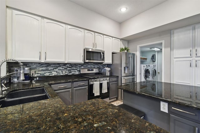 kitchen featuring stainless steel appliances, separate washer and dryer, dark stone counters, white cabinets, and sink