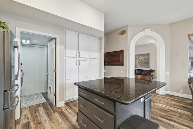 kitchen featuring dark stone countertops, a kitchen island, stainless steel refrigerator, white cabinetry, and dark wood-type flooring