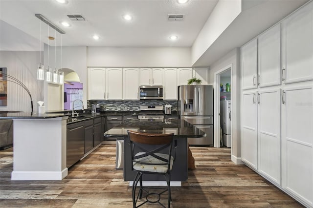 kitchen with stainless steel appliances, white cabinetry, hanging light fixtures, and a kitchen island