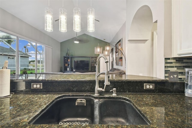 kitchen with lofted ceiling, dark stone countertops, pendant lighting, white cabinets, and sink