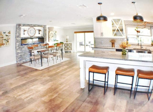 kitchen with a kitchen bar, sink, white cabinetry, hanging light fixtures, and light stone countertops