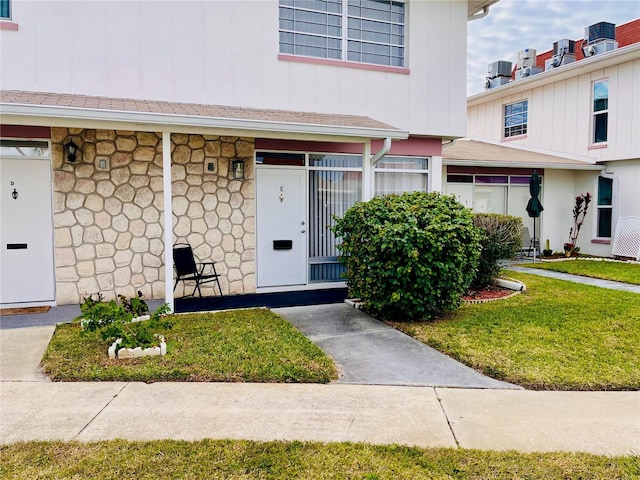 4352 Tahitian Gardens Cir Unit E, Holiday, FL 34691 - doorway to property featuring board and batten siding, stone siding, and a lawn