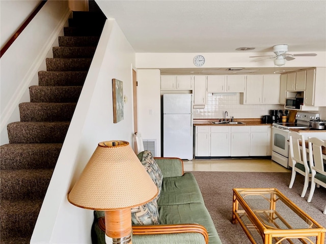 kitchen with white appliances, tasteful backsplash, white cabinets, a ceiling fan, and a sink