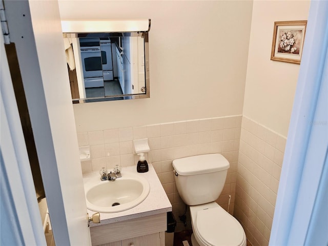 half bathroom with toilet, a wainscoted wall, tile walls, and vanity