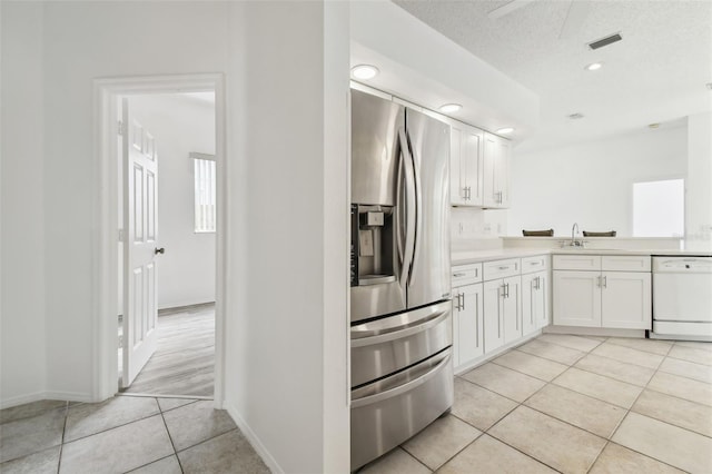 kitchen featuring stainless steel fridge, light tile patterned flooring, dishwasher, a textured ceiling, and white cabinets