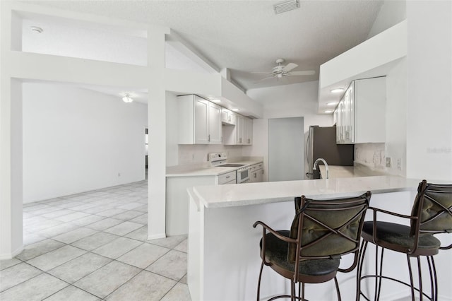 kitchen with a breakfast bar, stainless steel fridge, kitchen peninsula, and white range with electric cooktop