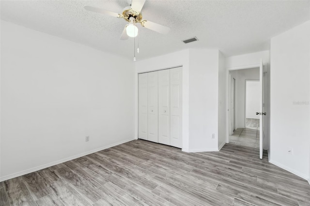 unfurnished bedroom featuring ceiling fan, a closet, a textured ceiling, and light hardwood / wood-style flooring