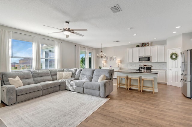 living room with a textured ceiling, ceiling fan with notable chandelier, and light hardwood / wood-style flooring