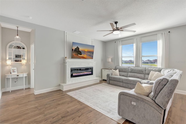 living room with ceiling fan, wood-type flooring, a fireplace, and a textured ceiling