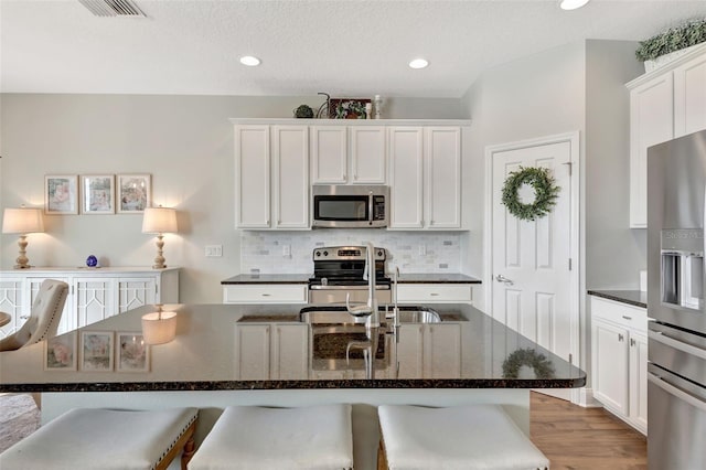 kitchen featuring white cabinetry, a center island with sink, stainless steel appliances, decorative backsplash, and a breakfast bar