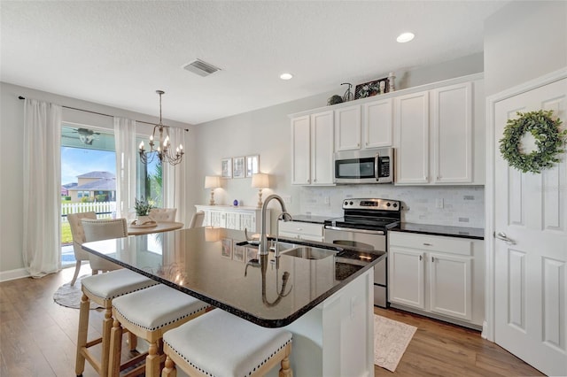 kitchen featuring a center island with sink, sink, an inviting chandelier, white cabinetry, and appliances with stainless steel finishes