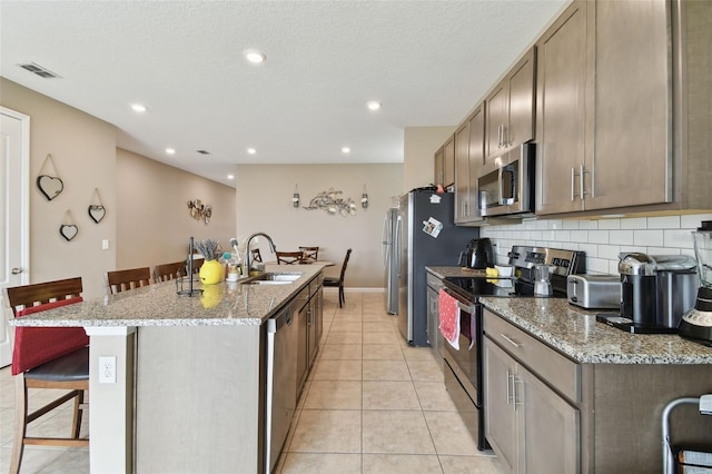 kitchen featuring light tile patterned floors, a kitchen bar, a center island with sink, stainless steel appliances, and sink