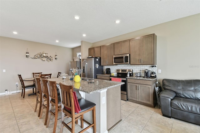 kitchen featuring a center island with sink, light tile patterned flooring, a kitchen breakfast bar, stainless steel appliances, and light stone counters