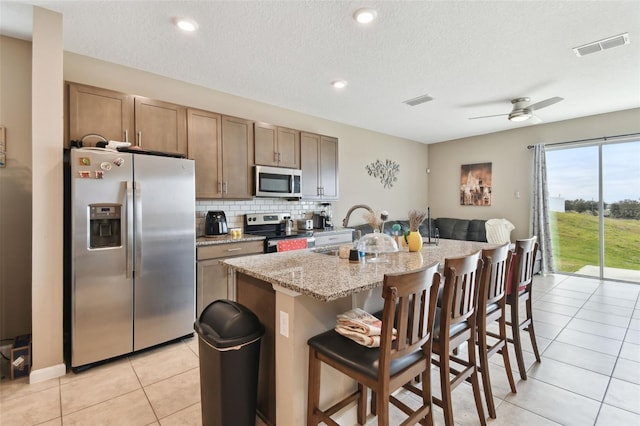 kitchen with ceiling fan, sink, appliances with stainless steel finishes, an island with sink, and light tile patterned floors