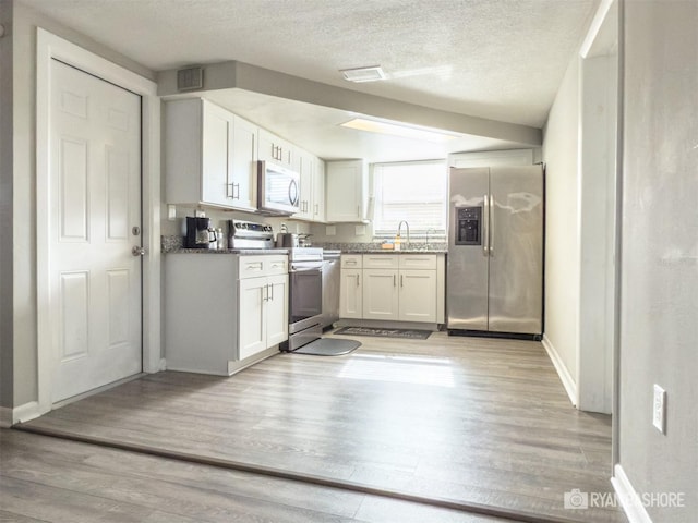 kitchen featuring a textured ceiling, stainless steel appliances, light hardwood / wood-style floors, and white cabinetry