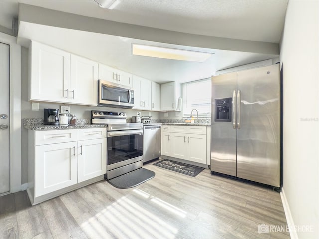 kitchen featuring light stone counters, white cabinetry, appliances with stainless steel finishes, and light wood-type flooring