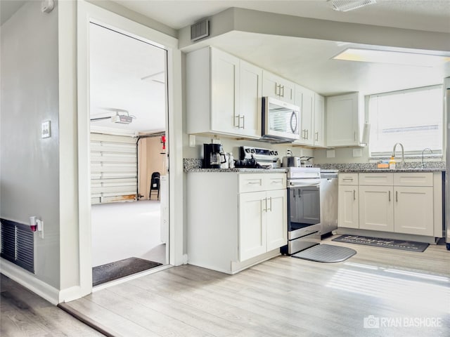 kitchen with light hardwood / wood-style floors, appliances with stainless steel finishes, light stone countertops, white cabinets, and sink