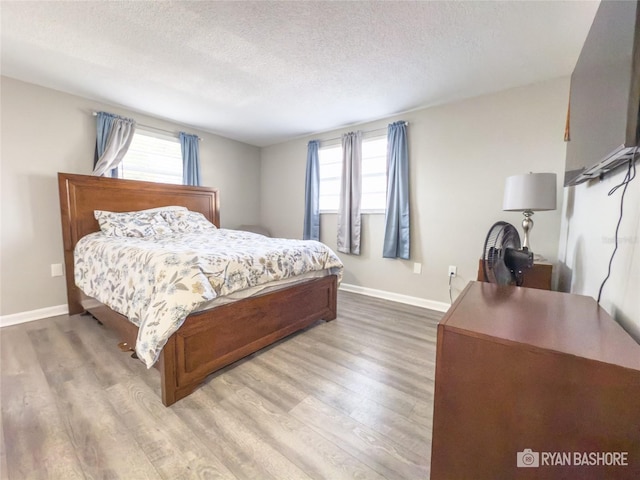 bedroom featuring light hardwood / wood-style flooring, a textured ceiling, and multiple windows