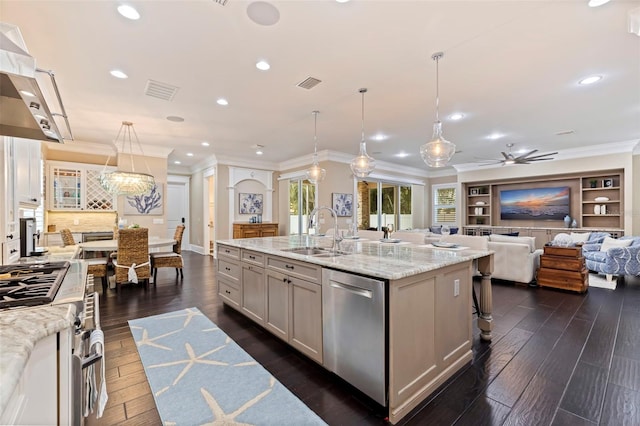 kitchen with an island with sink, stainless steel appliances, decorative light fixtures, light stone countertops, and sink