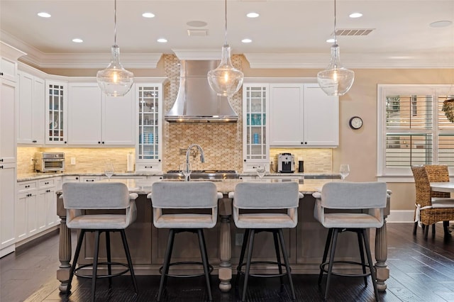 310 8th Ave N, Saint Petersburg, FL 33701 - kitchen with wall chimney exhaust hood, ornamental molding, an island with sink, white cabinetry, and light stone countertops