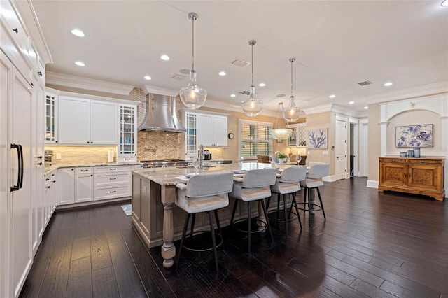 310 8th Ave N, Saint Petersburg, FL 33701 - kitchen featuring wall chimney range hood, ornamental molding, a kitchen island with sink, decorative backsplash, and light stone countertops