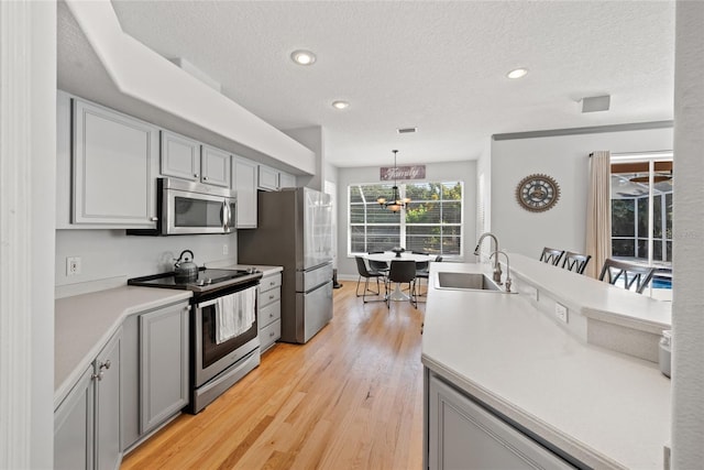 kitchen with sink, gray cabinetry, stainless steel appliances, light hardwood / wood-style floors, and decorative light fixtures