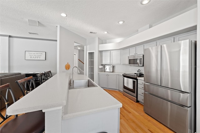 kitchen featuring appliances with stainless steel finishes, sink, a breakfast bar area, kitchen peninsula, and light hardwood / wood-style flooring