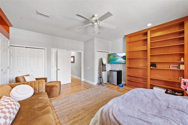 bedroom with two closets, a textured ceiling, and light wood-type flooring