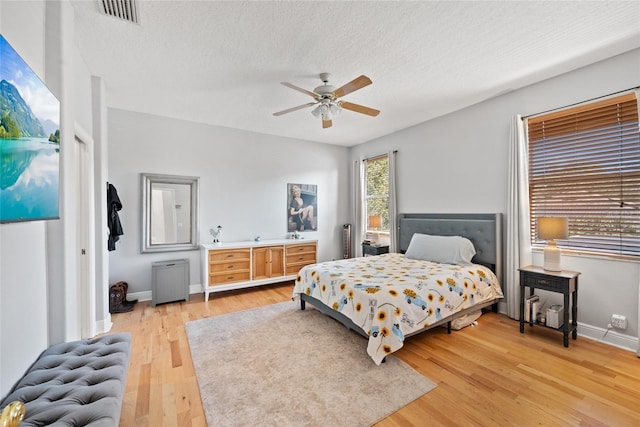 bedroom with ceiling fan, light hardwood / wood-style floors, and a textured ceiling