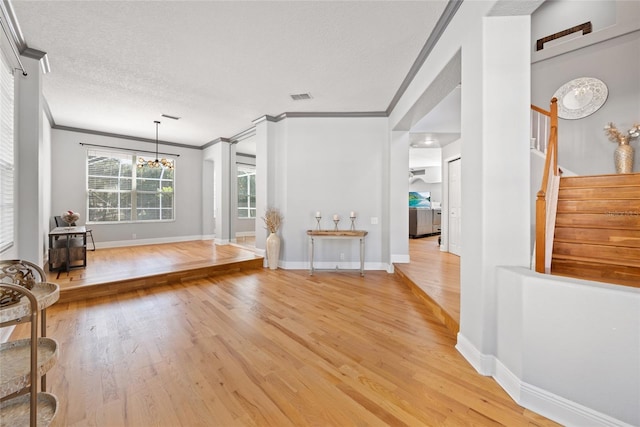 unfurnished living room featuring hardwood / wood-style flooring, ornamental molding, an inviting chandelier, and a textured ceiling