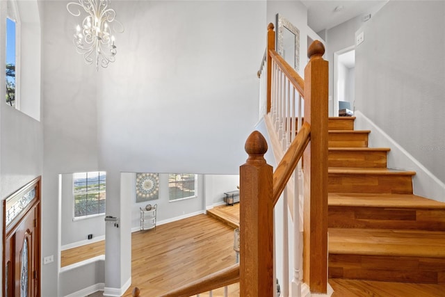 staircase with a towering ceiling, hardwood / wood-style floors, and a notable chandelier