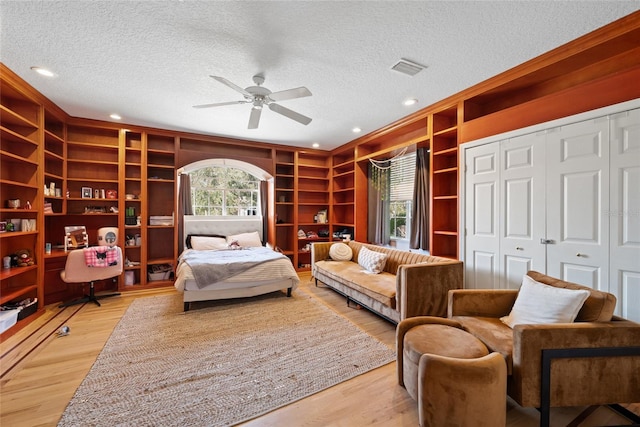 living area with ceiling fan, built in features, a textured ceiling, and light wood-type flooring