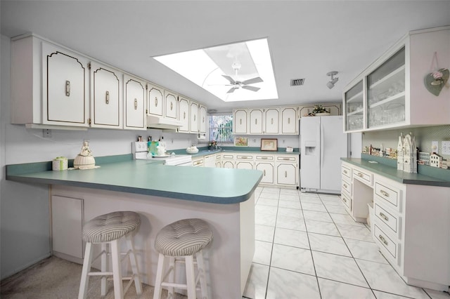 kitchen featuring a breakfast bar, kitchen peninsula, a skylight, white refrigerator with ice dispenser, and range