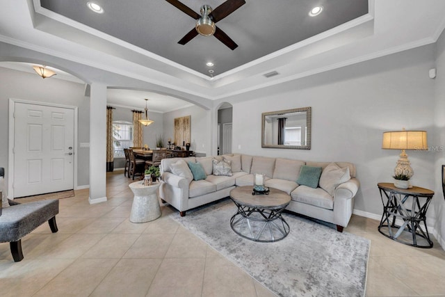 living room featuring ceiling fan, light tile patterned floors, crown molding, and a raised ceiling