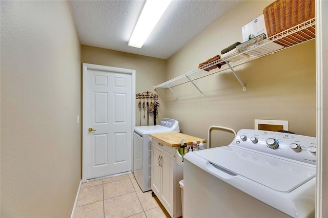 laundry room with light tile patterned floors, washing machine and dryer, a textured ceiling, and cabinets