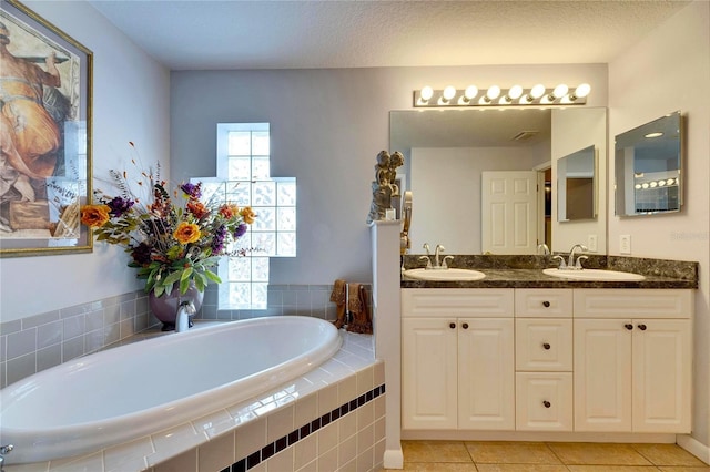 bathroom with a textured ceiling, tile patterned flooring, tiled tub, and vanity