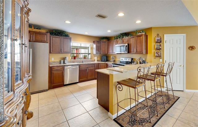 kitchen with appliances with stainless steel finishes, a kitchen bar, sink, kitchen peninsula, and light tile patterned floors